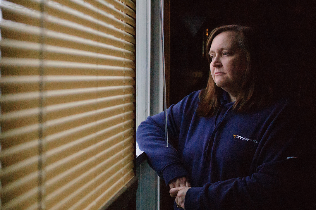 Susan stands in her living room which overlooks the hydraulic fracking operation behind her home. "It's pretty loud. I'm up constantly. I have a sound machine to try and drown it out, but it can't really be drowned out, " said Susan referring to the fracking operation behind her home. "Ironically, I work in a sleep center." (Photograph by Raven Pettigrew)